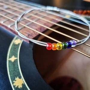 Peut inclure: Un lien de guitare en corde avec des perles de couleur arc-en-ciel, rouge, orange, jaune, vert, bleu et violet, sur une corde de guitare argentée.