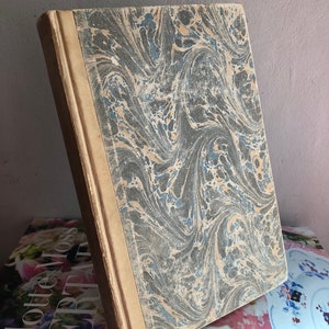 May include: A vintage book with a marbled cover in shades of gray, blue, and beige. The book is bound in brown leather and has a spine with raised lettering.