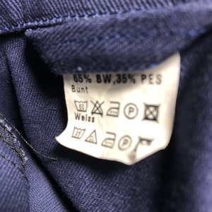 May include: A white care label with black text and symbols. The text reads "65% BW, 35% PES Bunt Weiss". The symbols indicate washing instructions, including machine wash at 60 degrees Celsius, do not bleach, tumble dry low, iron at medium heat, and do not dry clean.
