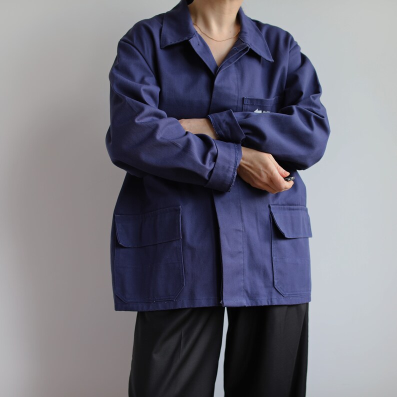 May include: A dark blue work jacket with two large pockets on the front. The jacket has a button-up closure and a collar.