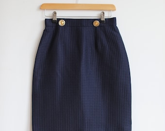 May include: A navy blue skirt with a textured pattern and gold buttons. The skirt is knee-length and has a straight silhouette.