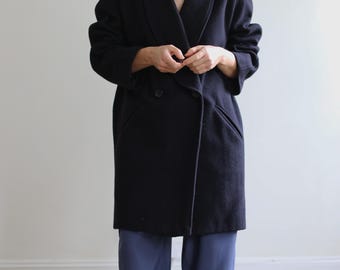 Könnte beinhalten: Ein marineblauer, doppelreihiger Mantel mit breitem Revers und zwei Vordertaschen. Der Mantel ist knielang und scheint aus einem dicken, warmen Material zu sein. Die Person trägt eine blaue Hose.