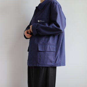 May include: A dark blue work jacket with a patch on the left chest that reads "S&uuml;dtiroler Wasserrettung". The jacket has a large pocket on the left side and a button-up closure.