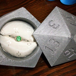 May include: A gray, 3D printed ring box shaped like a 20-sided die, with a green gemstone ring inside.