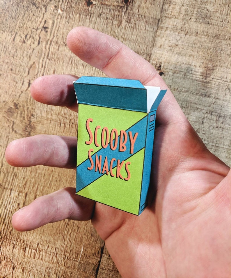 May include: A small cardboard box with a green and blue design. The box has the words "Scooby Snacks" printed on it in orange letters.