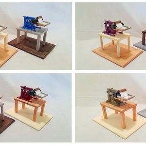 May include: Six miniature printing presses on wooden bases. The presses are painted in various colors, including blue, red, purple, and green. The bases are painted in various colors, including brown, white, and gray.