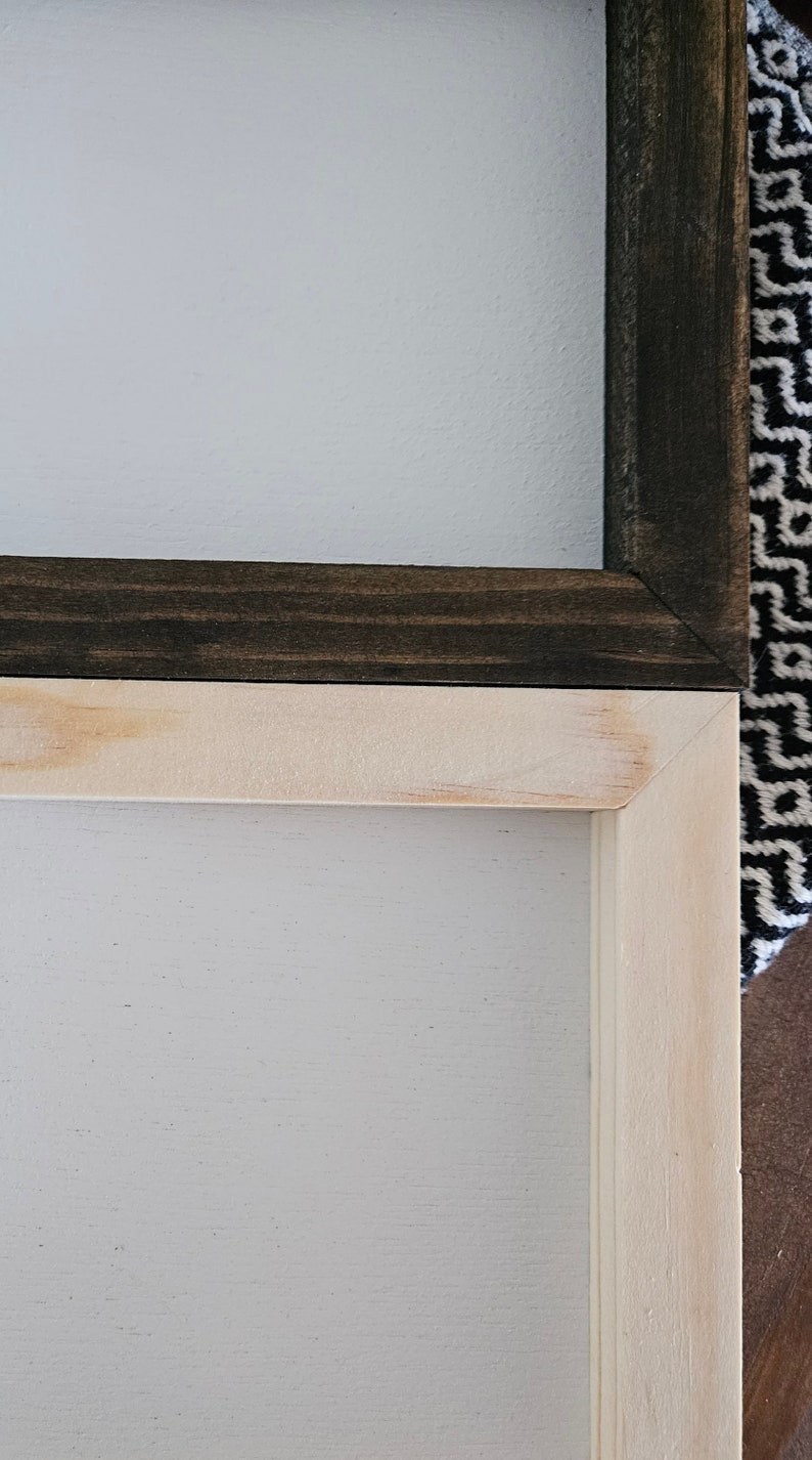 May include: Two wooden picture frames, one with a dark brown stain and one with a light wood stain. The frames are stacked on top of each other.