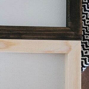 May include: Close-up of two wooden framed signs. One frame is stained dark brown, the other is natural wood. Both signs have a white painted surface. The frames are joined at a 90-degree angle.