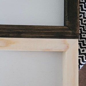 May include: Two rectangular wooden frames with mitered corners. The top frame is finished in a dark brown stain, while the bottom frame is made of light, natural-colored wood. Both frames feature a smooth, flat surface and a clean, simple construction.