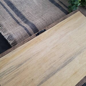 May include: The back of a wooden sign with a brown stain. The sign has a metal hanger attached to the back.