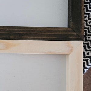 May include: Close-up of two wooden framed signs. One frame is stained dark brown, the other is natural wood with a light stain. Both have a white painted surface. The frames are joined at a corner.