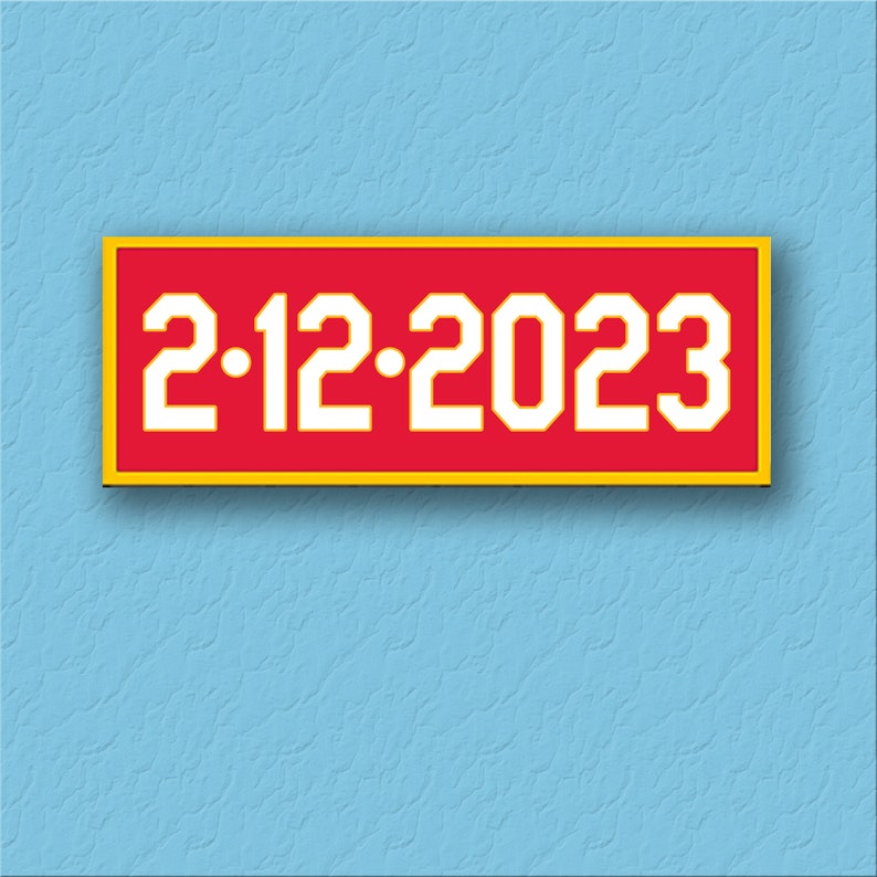 Op de afbeelding: Een rechthoekige rode patch met een gele rand en witte tekst die "2.12.2023" luidt.