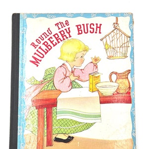 Könnte beinhalten: Ein altes Kinderbuch mit dem Titel "Round the Mulberry Bush" mit einer farbenfrohen Illustration eines Mädchens in einem rosa Kleid, das an einem Tisch mit einem Vogelkäfig, einer Schüssel und einem Krug sitzt. Der Buchumschlag hat einen blauen Hintergrund mit weißen Blumen.