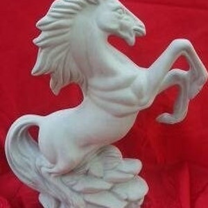 Op de afbeelding: Witte keramische paardensculptuur in een opgerichte houding met een vloeiende manen en staart. Het paard staat op een rotsachtige basis.