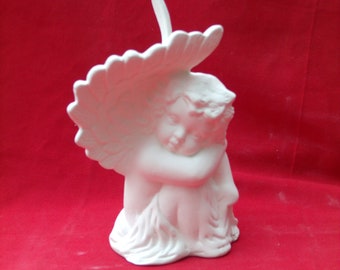 Może przedstawiać: Biała ceramiczna figurka śpiącego anioła z skrzydłami. Anioł trzyma głowę w dłoniach i ma spokojny wyraz twarzy.