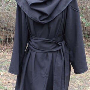 May include: A black hooded coat with a long, flowing design. The coat has a wide, gathered collar and a belt that ties at the waist. The coat is made of a soft, drapey fabric.