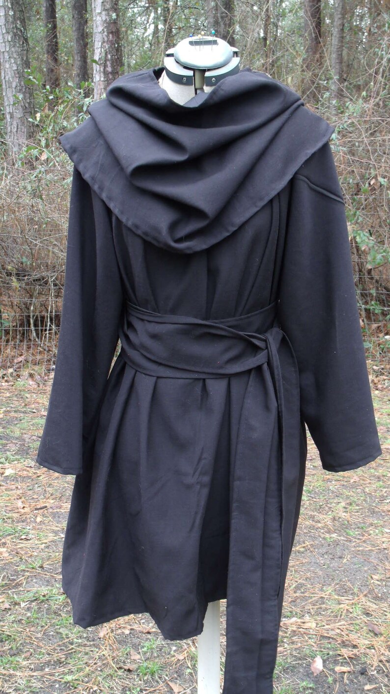 May include: A black hooded coat with a long, flowing design. The coat has a wide, gathered collar and a belt that ties at the waist. The coat is made of a soft, drapey fabric.