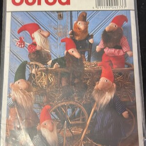 May include: A Burda sewing pattern with images of gnome dolls, each with a red hat and beard, in different outfits. The pattern includes measurements of 50 cm and 40 cm.