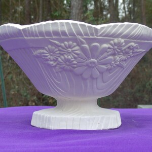 May include: White ceramic bowl with a floral design. The bowl has a wide, shallow base and a flared rim. The floral design is embossed on the bowl and features a variety of flowers and leaves.