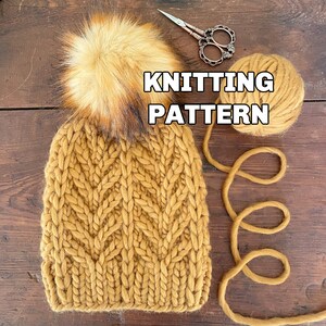 May include: A knitted beanie hat in a mustard yellow color with a large brown and black faux fur pom pom on top. The hat is made with a cable knit stitch and is laying on a wooden surface with a ball of yarn and a pair of scissors. The text "KNITTING PATTERN" is written in white letters on a black background.