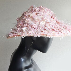 Puede incluir: Un sombrero de ala ancha con un dise&ntilde;o floral rosa y blanco. El sombrero est&aacute; decorado con cuentas de imitaci&oacute;n de perlas y tiene una est&eacute;tica delicada y femenina.