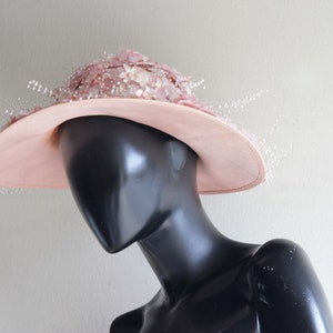 Puede incluir: Un sombrero rosa de ala ancha con un delicado dise&ntilde;o floral. El sombrero est&aacute; adornado con peque&ntilde;as cuentas blancas que cuelgan del ala.