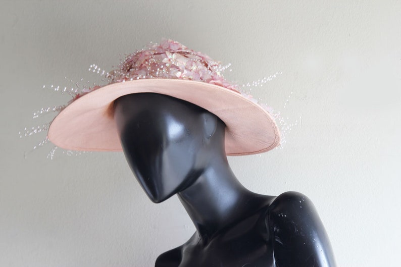 Puede incluir: Un sombrero rosa de ala ancha con un delicado dise&ntilde;o floral. El sombrero est&aacute; adornado con peque&ntilde;as cuentas blancas que cuelgan del ala.