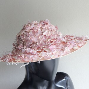 Puede incluir: Un sombrero de ala ancha con una base rosa y una corona cubierta de delicadas flores rosas y cuentas de perlas.