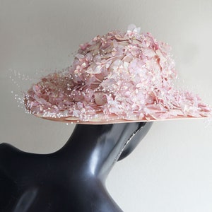 Puede incluir: Un sombrero rosa con un ala ancha y un dise&ntilde;o floral. El sombrero est&aacute; decorado con peque&ntilde;as cuentas blancas y tiene un velo delicado.