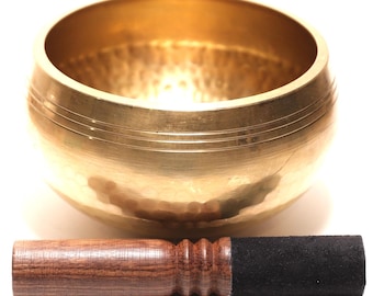 Könnte beinhalten: Eine goldene Klangschale mit einem Schlägel aus Holz und Filz. Die Schale hat eine gehämmerten Textur und ist rund mit einer weiten Öffnung. Der Schlägel ist braun mit einem schwarzen Filzende. Auf weißem Hintergrund.