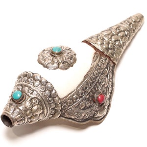 Peut inclure: Objet décoratif en forme de corne, orné de métal argenté, de motifs floraux et de pierres précieuses turquoise et rouges. L'intérieur de la corne est blanc, et l'extérieur présente des textures détaillées, possiblement pour un usage cérémoniel.