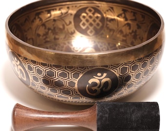 Könnte beinhalten: Eine bronzene Klangschale mit aufwendigen geätzten Mustern und einem Holzschlägel. Die Schale hat ein geometrisches Design und das Om-Symbol. Der Schlägel hat einen Holzgriff und eine schwarze Wildleder-Schlagfläche. Ein Meditationswerkzeug.