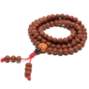 May include: A brown wooden mala bead necklace with a red string tassel and a small wooden bead accent.