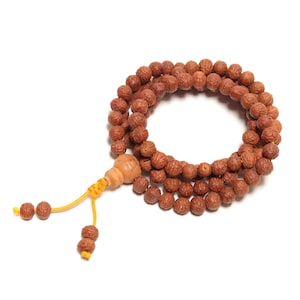 May include: A brown wooden mala bead necklace with a small wooden bead at the end. The necklace is made of 108 beads and is used for meditation and prayer.