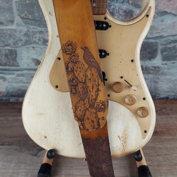 Correa de guitarra de cuero Desert Crow - Marrón antiguo. Correa para instrumento hecha a mano con cuervo, cactus y duna de arena. Tamaño ajustable para una altura personalizada.