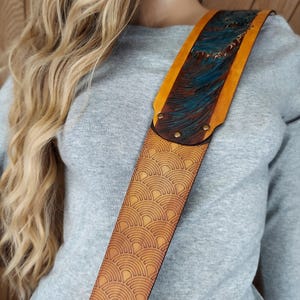 Puede incluir: Correa de guitarra de cuero marr&oacute;n claro con un dise&ntilde;o &uacute;nico. Presenta un patr&oacute;n repetido de abanicos y una secci&oacute;n superior con un dise&ntilde;o de olas azules y marrones. Los bordes son amarillos y la correa est&aacute; asegurada con remaches. Accesorio musical.