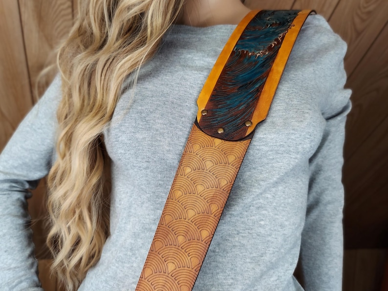 Puede incluir: Correa de guitarra de cuero marr&oacute;n claro con un dise&ntilde;o &uacute;nico. Presenta un patr&oacute;n repetido de abanicos y una secci&oacute;n superior con un dise&ntilde;o de olas azules y marrones. Los bordes son amarillos y la correa est&aacute; asegurada con remaches. Accesorio musical.