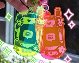 May include: Two translucent keychains with a cartoon design. The keychain on the left is green and features a cartoon cat. The keychain on the right is pink and features a cartoon bunny. Both keychains have a cartoon mailbox and the text "きみと" on them.