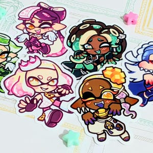 May include: A collection of seven colorful character stickers. Each sticker features a unique cartoon character with distinct features and outfits. The stickers are arranged on a white background with decorative frames and star-shaped embellishments.