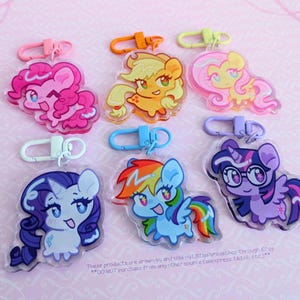 May include: Six acrylic keychains featuring cartoon pony characters with colorful manes and tails. Each charm is attached to a plastic lobster clasp in a matching color, including pink, orange, yellow, white, blue, and purple hardware.