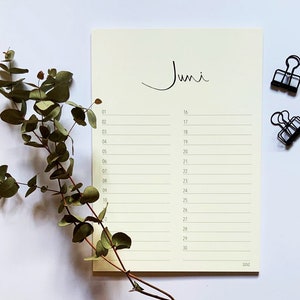 Può includere: Un planner mensile color crema con la parola "Juni" scritta in corsivo nero in alto. Il planner ha una griglia di numeri da 1 a 30, con righe per scrivere note. Due graffette nere sono su una superficie bianca.