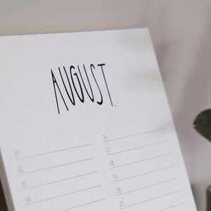 May include: A white calendar with the word "AUGUST" written in black ink. The calendar has lines for each day of the month, starting with the 16th.
