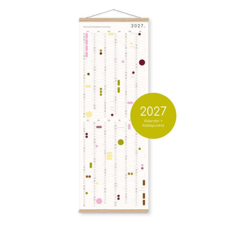 K&ouml;nnte beinhalten: Ein vertikaler Wandkalender f&uuml;r 2027, aufgeh&auml;ngt an einem hellen Holzrahmen. Das wei&szlig;e Papier zeigt ein Datumsraster mit verschiedenen farbigen Punkten und Formen zur Markierung. Ein gro&szlig;er olivgr&uuml;ner runder Aufkleber zeigt 2027 Kalender + Klebepunkte.