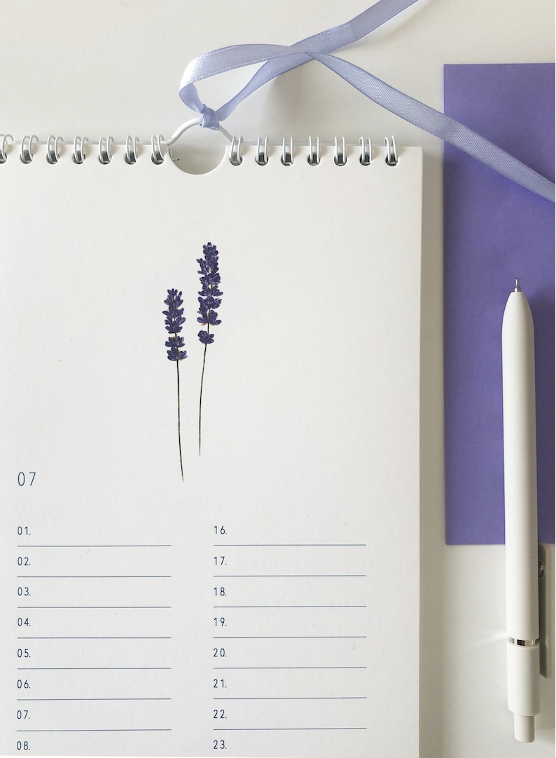 Pu&ograve; includere: Un calendario bianco con un fiore di lavanda pressato sulla pagina. Il calendario ha i numeri 07, 01, 02, 03, 04, 05, 06, 07, 08, 16, 17, 18, 19, 20, 21, 22 e 23 stampati su di esso.