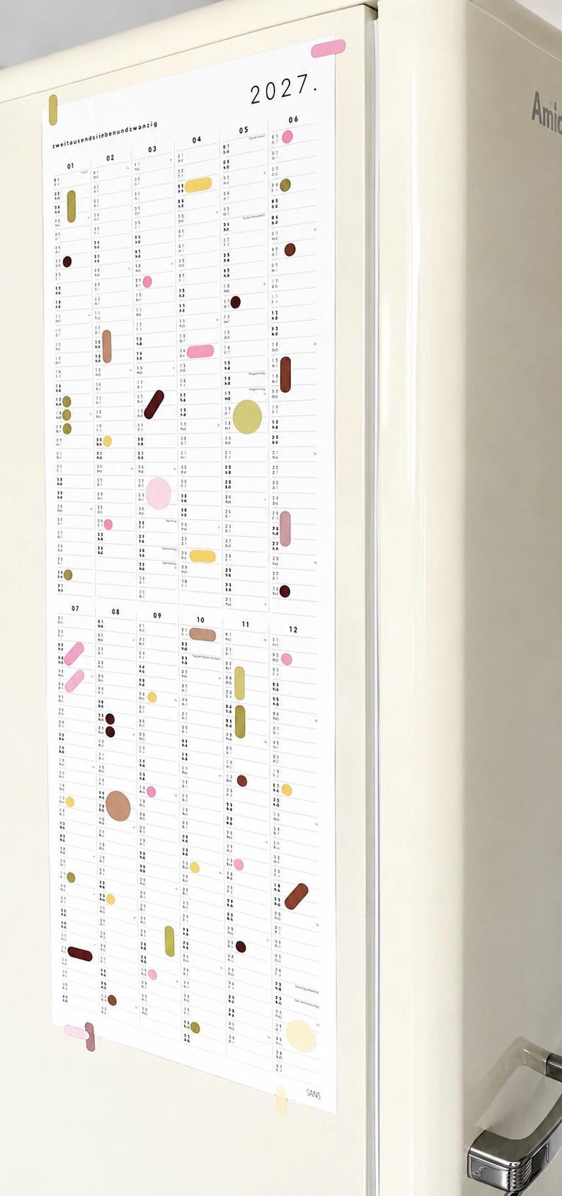 K&ouml;nnte beinhalten: Ein vertikaler Wandkalender f&uuml;r das Jahr 2027 mit dem Text "zweitausend siebenundzwanzig" und "2027." Der Kalender zeigt zw&ouml;lf Spalten f&uuml;r die Monate, die mit 01 bis 12 nummeriert sind und mit verschiedenen farbigen Formen verziert sind.