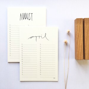 May include: Two blank calendar pages with handwritten month names "August" and "April". The pages are propped up on a wooden stand.