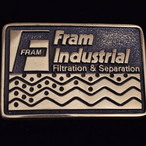 May include: A gold-colored metal belt buckle with the text "Fram Industrial Filtration & Separation" and a stylized wave design.