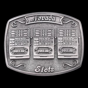 May include: Silver-colored belt buckle featuring three slot machines with the word "Nevada" above. Each machine displays "777" and "Dollars". The buckle also has the word "Slots" at the bottom.