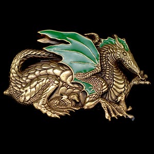 May include: A detailed, gold-colored dragon belt buckle with green enamel wings. The dragon is sculpted with intricate scales and features, set against a black background. The buckle is a fantasy-themed accessory.