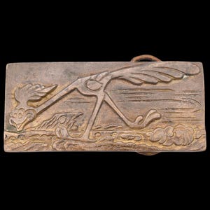 May include: A rectangular metal belt buckle featuring a detailed relief of the Road Runner cartoon character running across a desert landscape. The buckle has a bronze finish and a loop for attaching to a belt.
